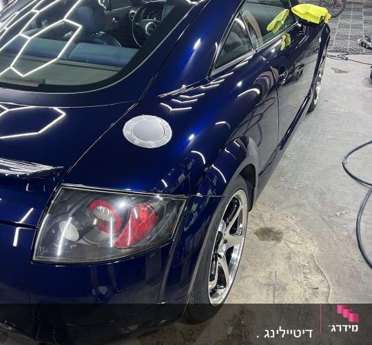 רכב כחול מבריק בתהליך דיטיילינג עם מגבת צהובה על המראה